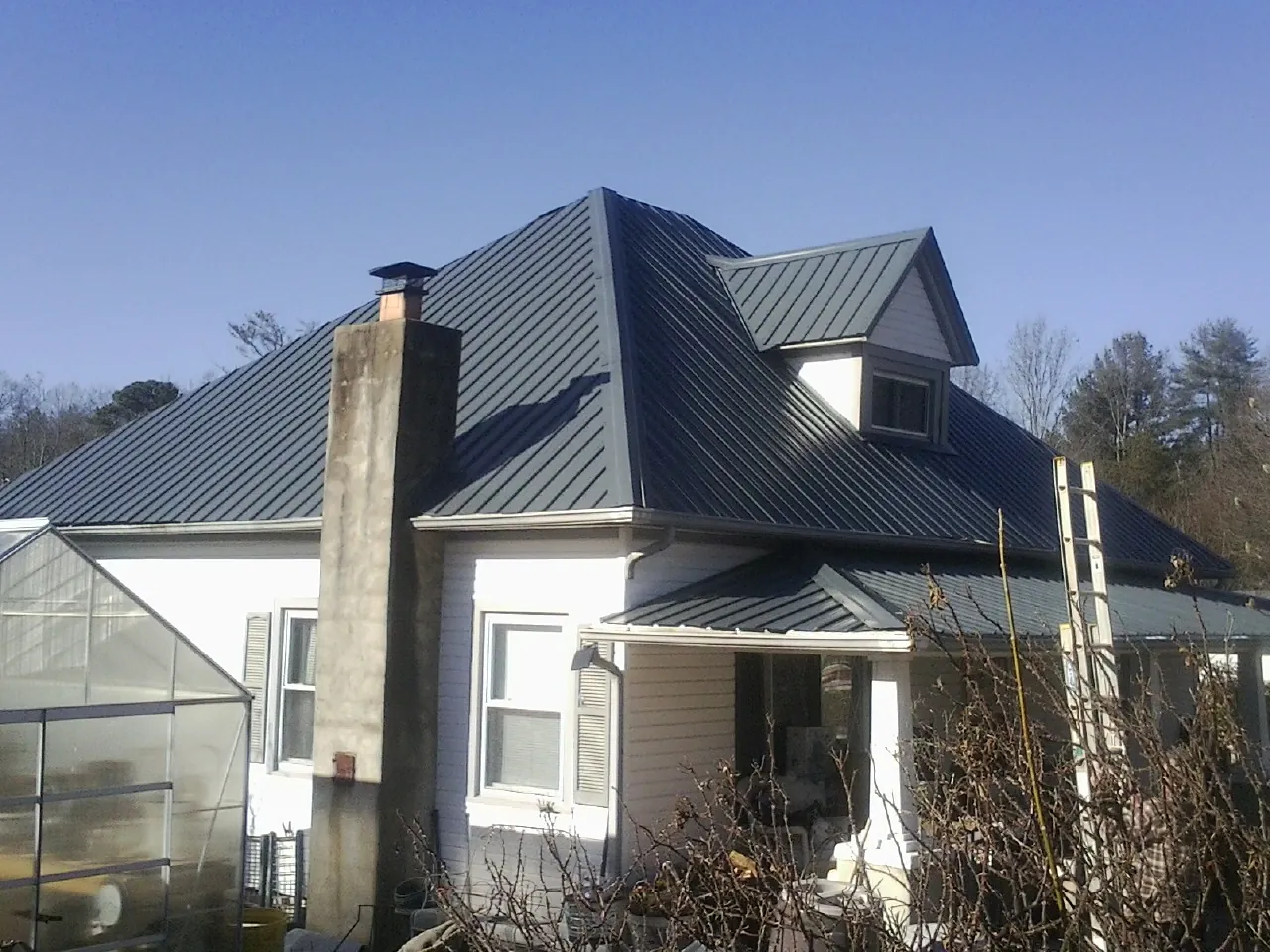 Dark blue standing seam metal roof on a white farmhouse with dormer — Slate & Tile Roof Repair by Roofing Brothers in Wylie