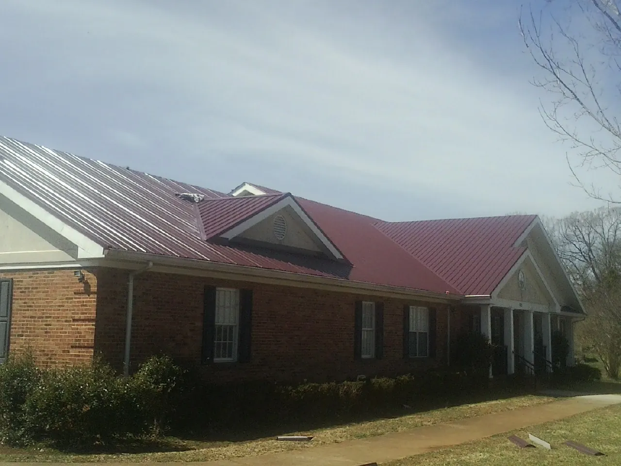 Red metal roof with gabled entries on a long brick building, from a Hail Damage Roof Repair job in Wylie