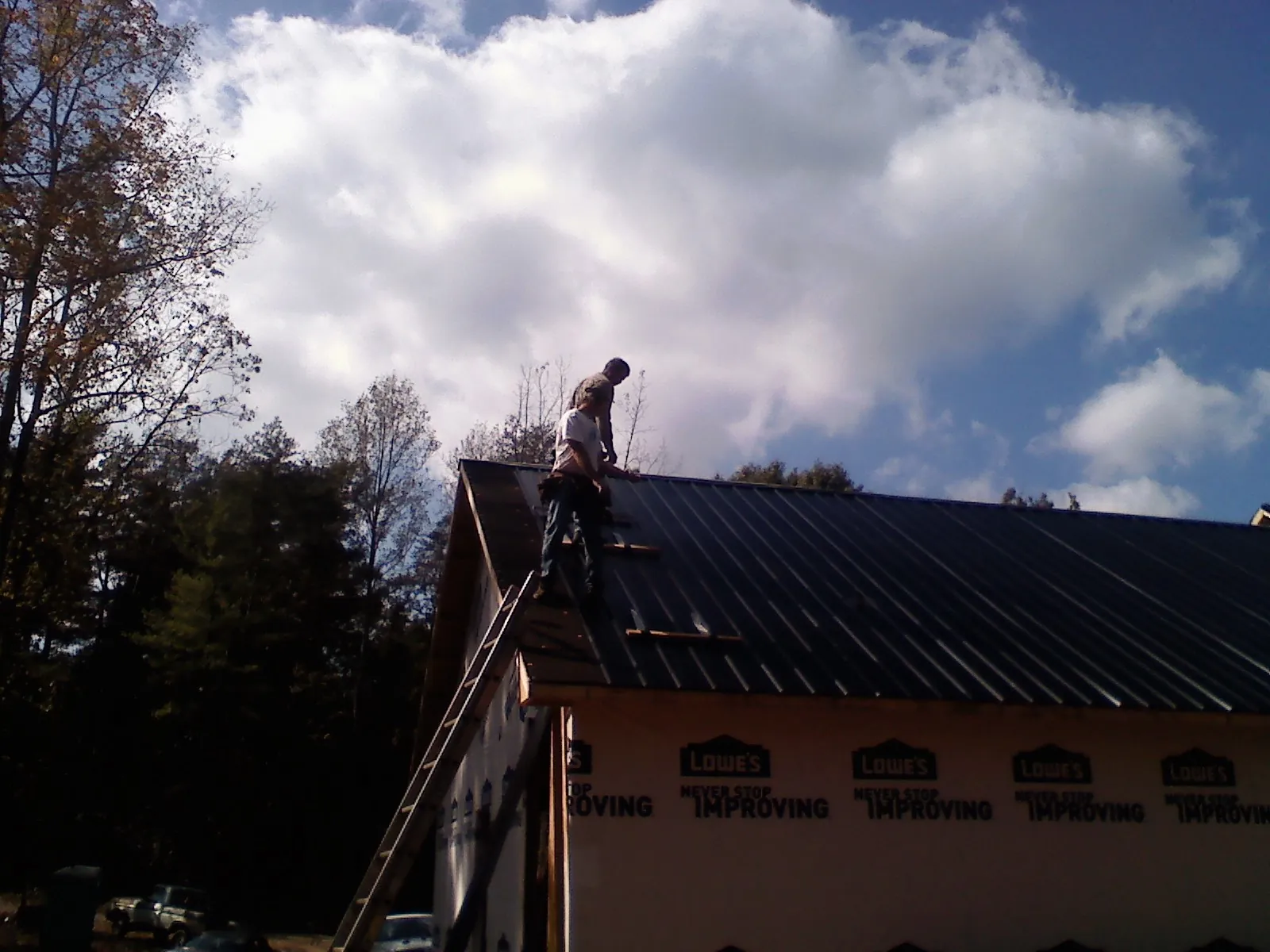 Roofer fastening dark metal panels high against a cloudy sky, from a Roof Inspection job in Wylie