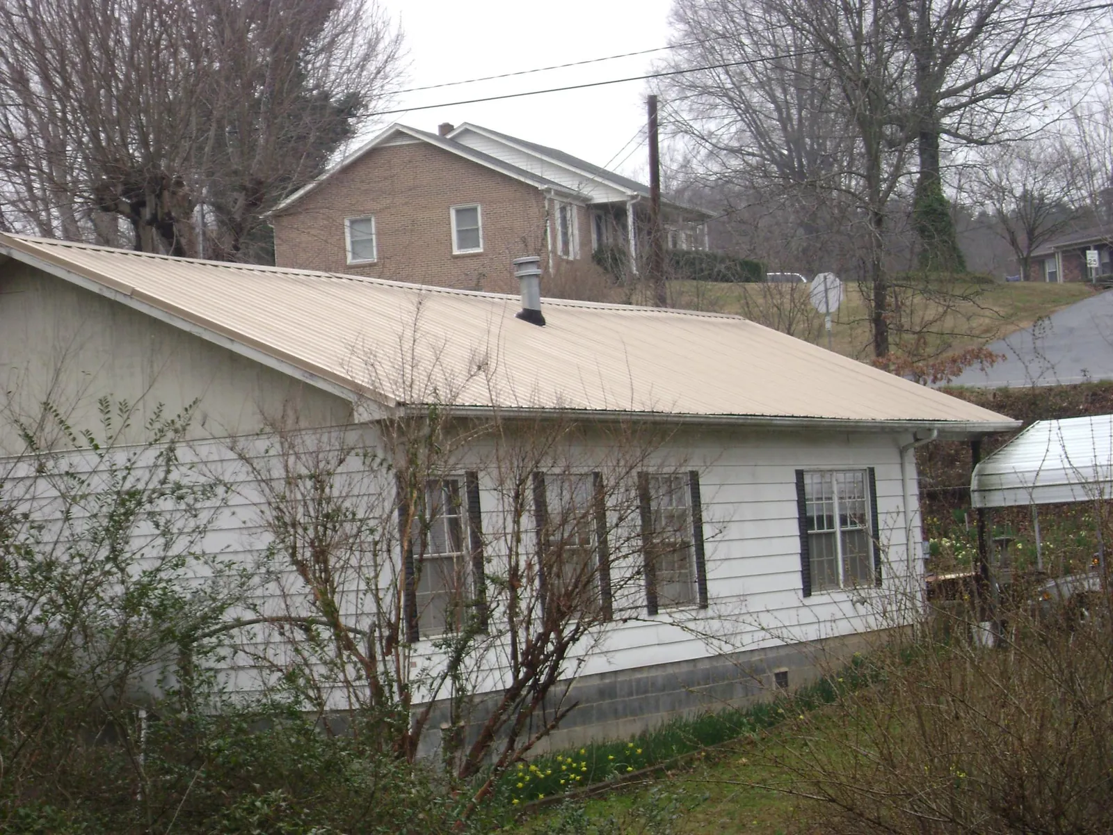 Tan metal roof on a white sided house set into a hillside — Commercial Roofing by Roofing Brothers in Wylie